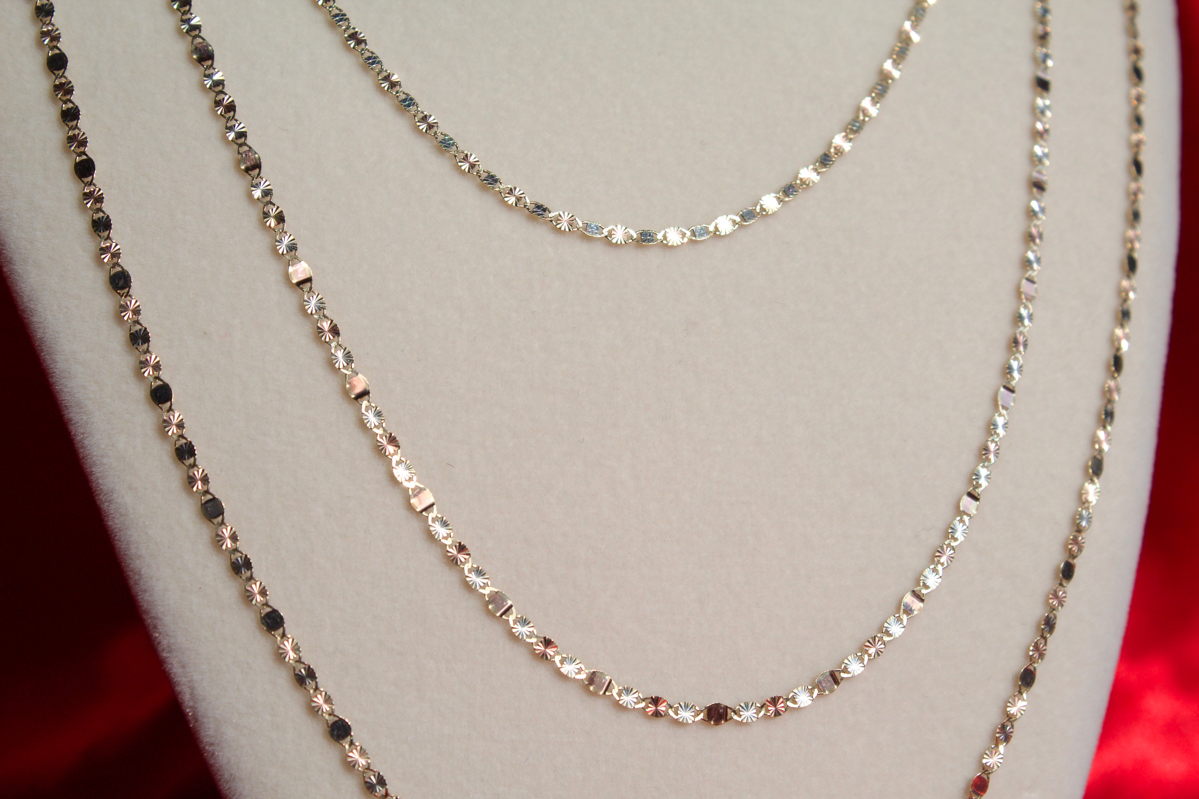 Three gold necklaces on a mannequin bust with a red background