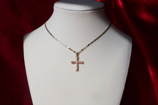 Gold cross necklace on a mannequin bust against a red satin background