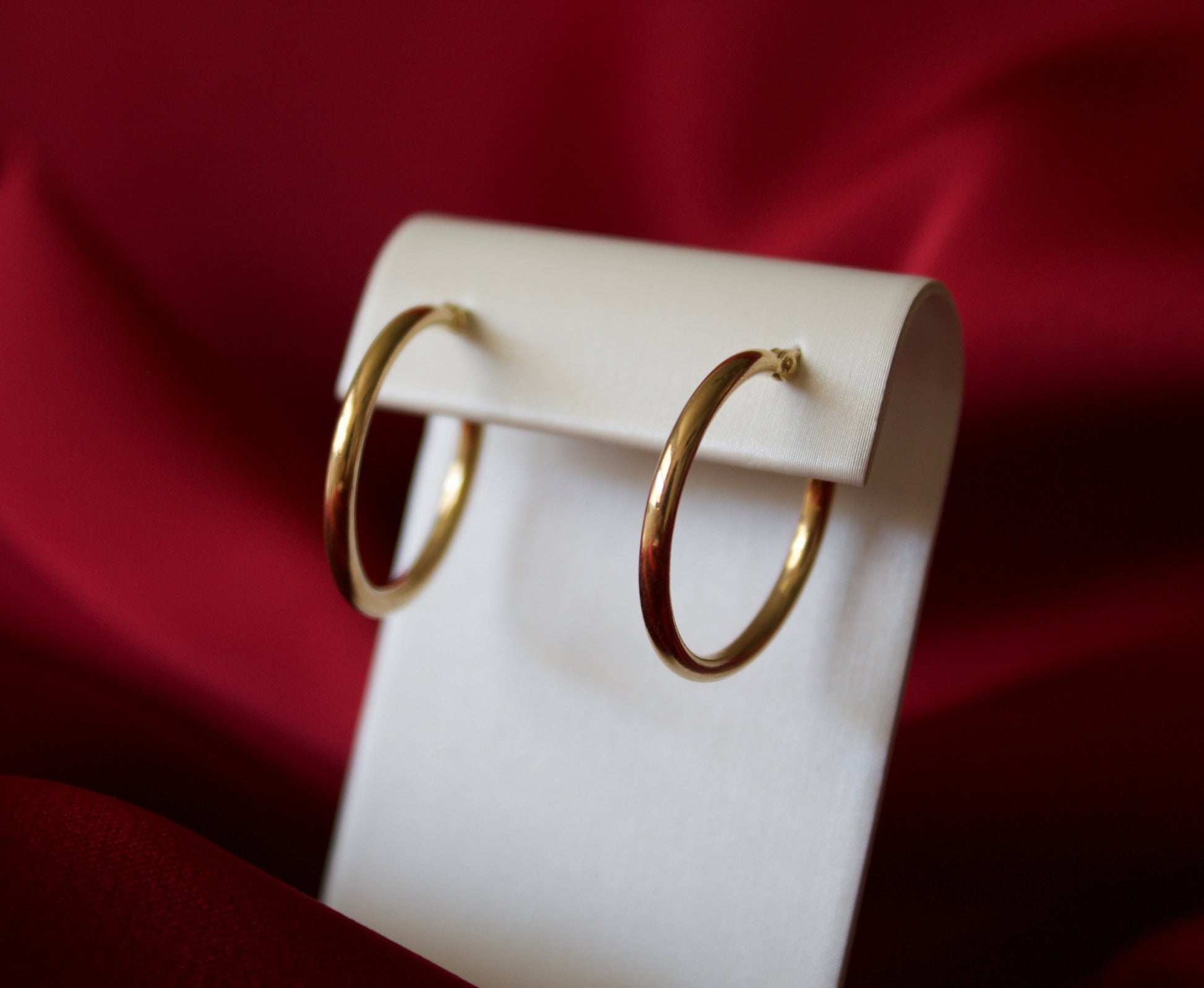 Gold hoop earrings on a white stand against a red fabric background